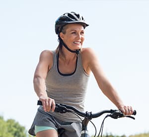 Mature woman riding on mountain bike in the park. Portrait of a happy senior woman riding bicycle in a park. Athletic woman wih helmet cycling and looking away.